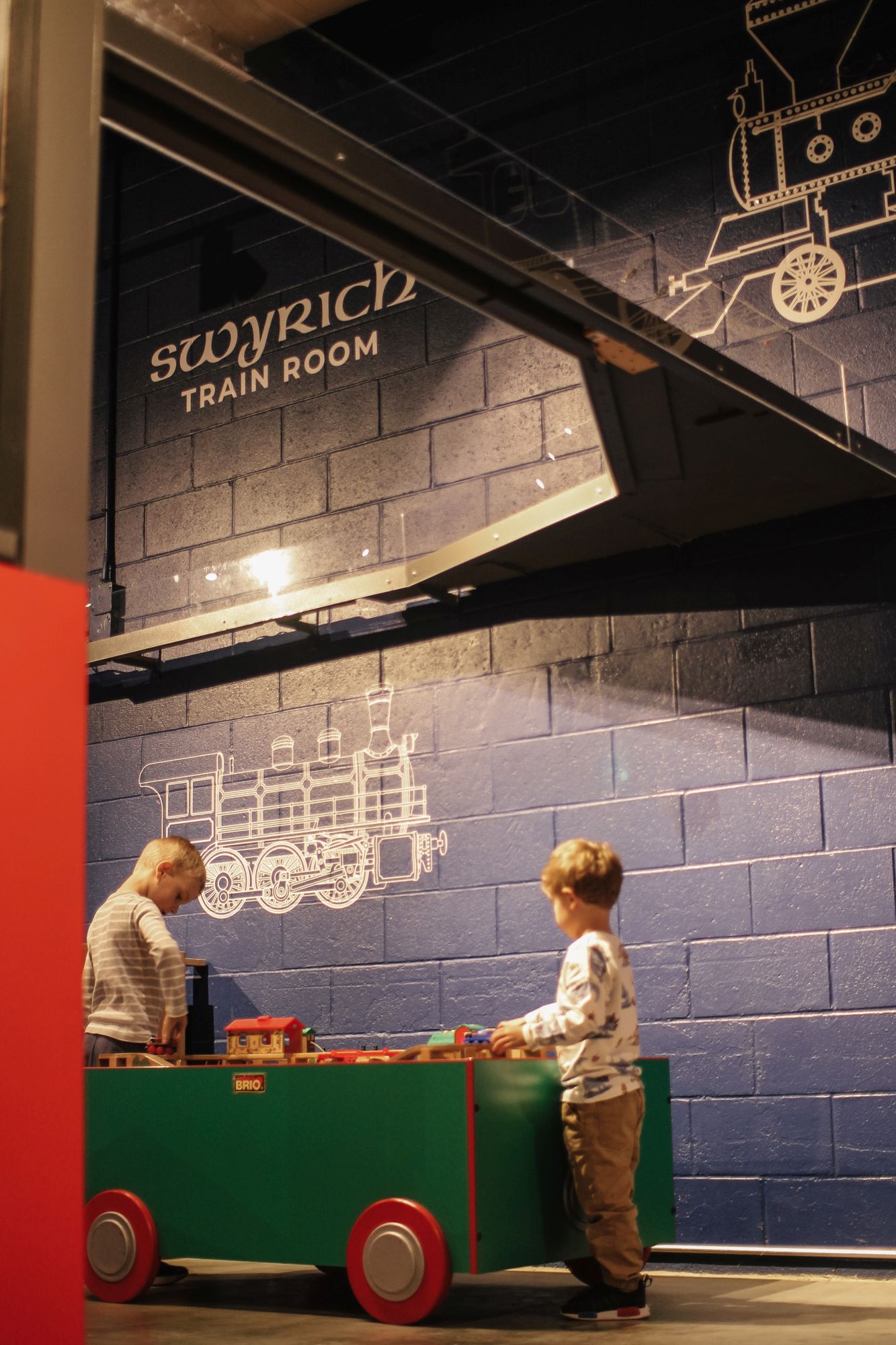 little boys playing at a wooden train table in the swyrich train room 